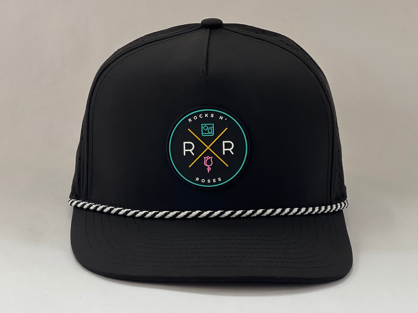 Image of a black golf hat with a teal, pink, and gold rubber Rocks N' Roses logo and a black and white diagonal rope accent.