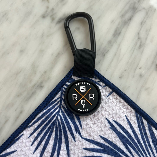 Close up photo of the Rocks N' Roses magnetic golf towel with a blue and white palm leaf pattern. Close up shows the waffle towel and magnet / carabiner for attaching to your golf bag or golf cart.