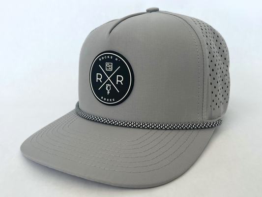 Close up shot of the Rocks N' Roses Gray Performance Golf Hat. This 100% polyester snapback hat is water resistant, offers some stretch and has that new school flat brim look. Also, it features a rubber logo and black and white rope that decorates the front brim. Laser cut venting for max breathability.
