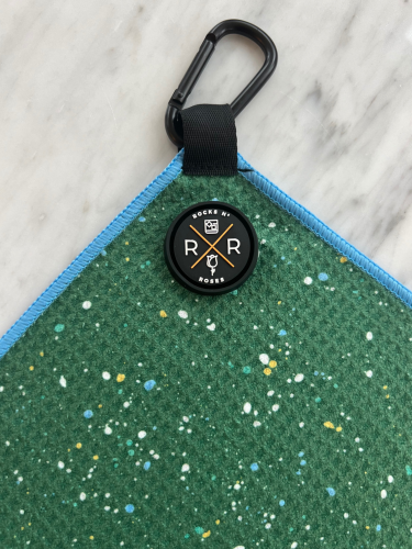 Close up shot of the Rocks N' Roses magnetic golf towel in green with a fun paint splatter pattern. Close up shows the magnet and carabiner for attaching to your golf bag.