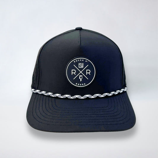Image of the Rocks N' Roses 5 panel black golf hat. This performance hat is made of 100% polyester and is water resistant and has some stretch. It features a black and white circular rubber logo on the front and a black and white rope.