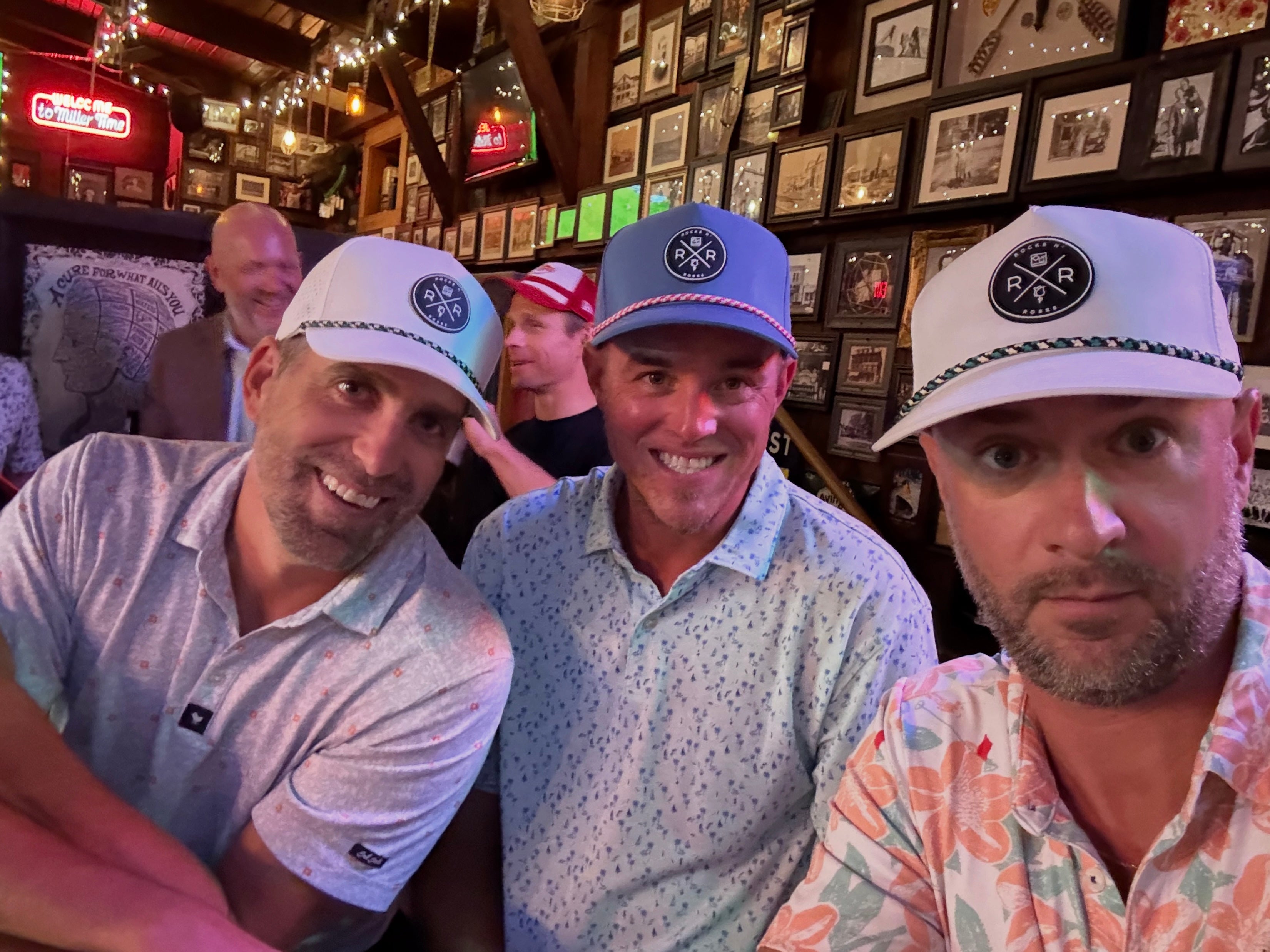 Photo of three men at a dive bar wearing each wearing the Rocks N' Roses Performance Golf Hat. White golf hat and blue steel golf hat.