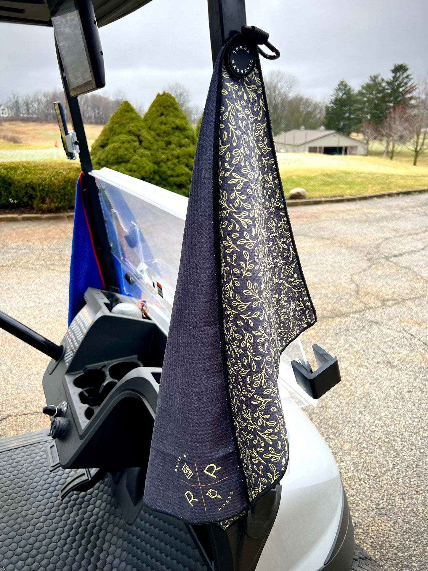 An image of the Rocks N' Roses black and golf magnetic golf towel attached magnetically to the metal frame of a golf cart for easy access during a round.