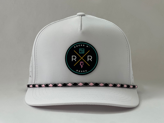 Image of a white golf hat made from 100% polyester with a teal, pink, and gold rubber Rocks N' Roses logo and a pink and black diamond rope.
