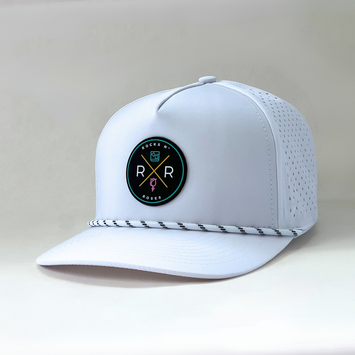 side shot of the Rocks N' Roses Tropical Sunset Golf Hat in White. This performance golf hat features a multi-color rubber logo and white rope with black accents.