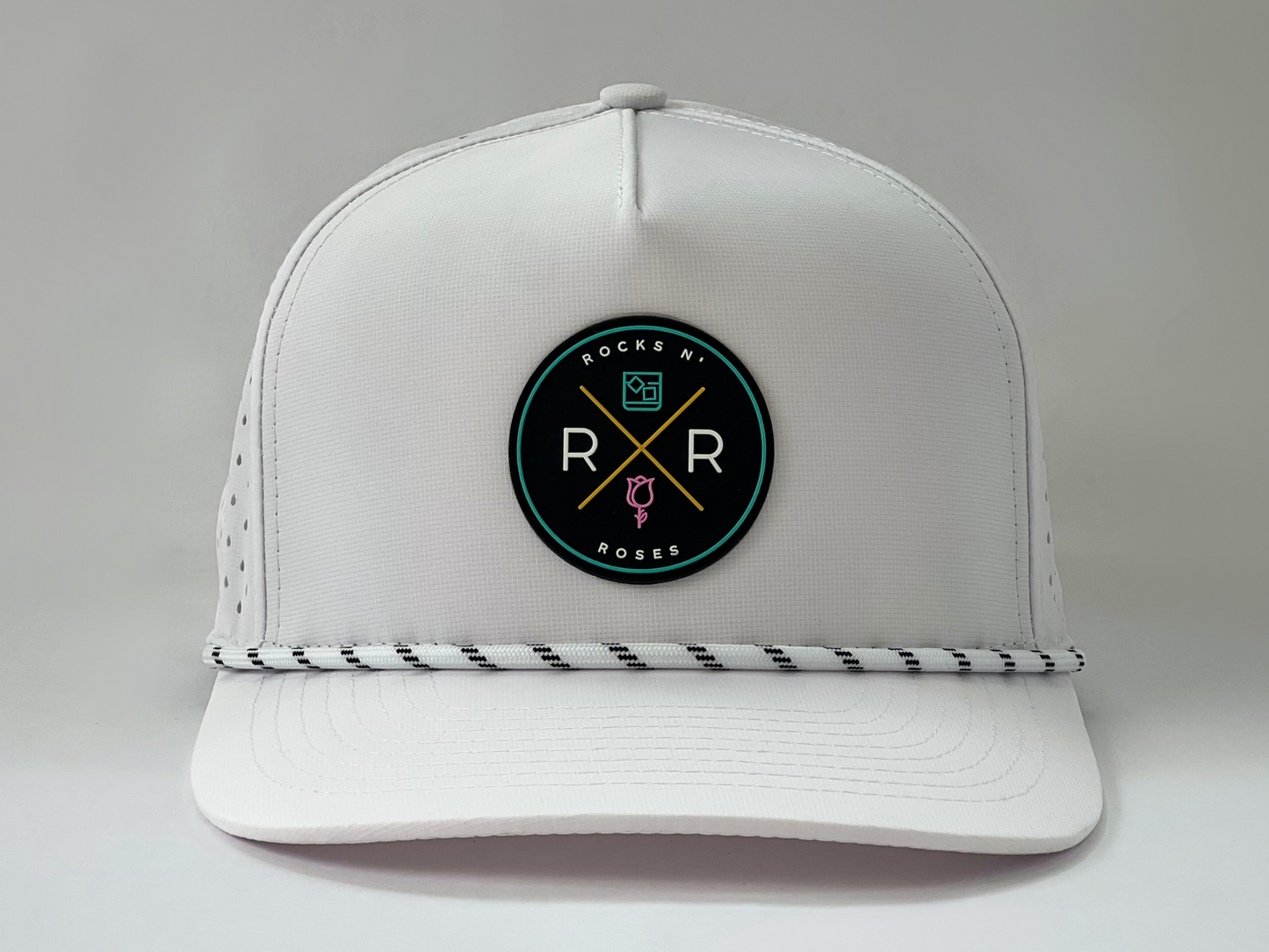 Image of a white golf hat made from 100% polyester with a teal, pink, and gold rubber Rocks N' Roses logo and white rope with a black accent.