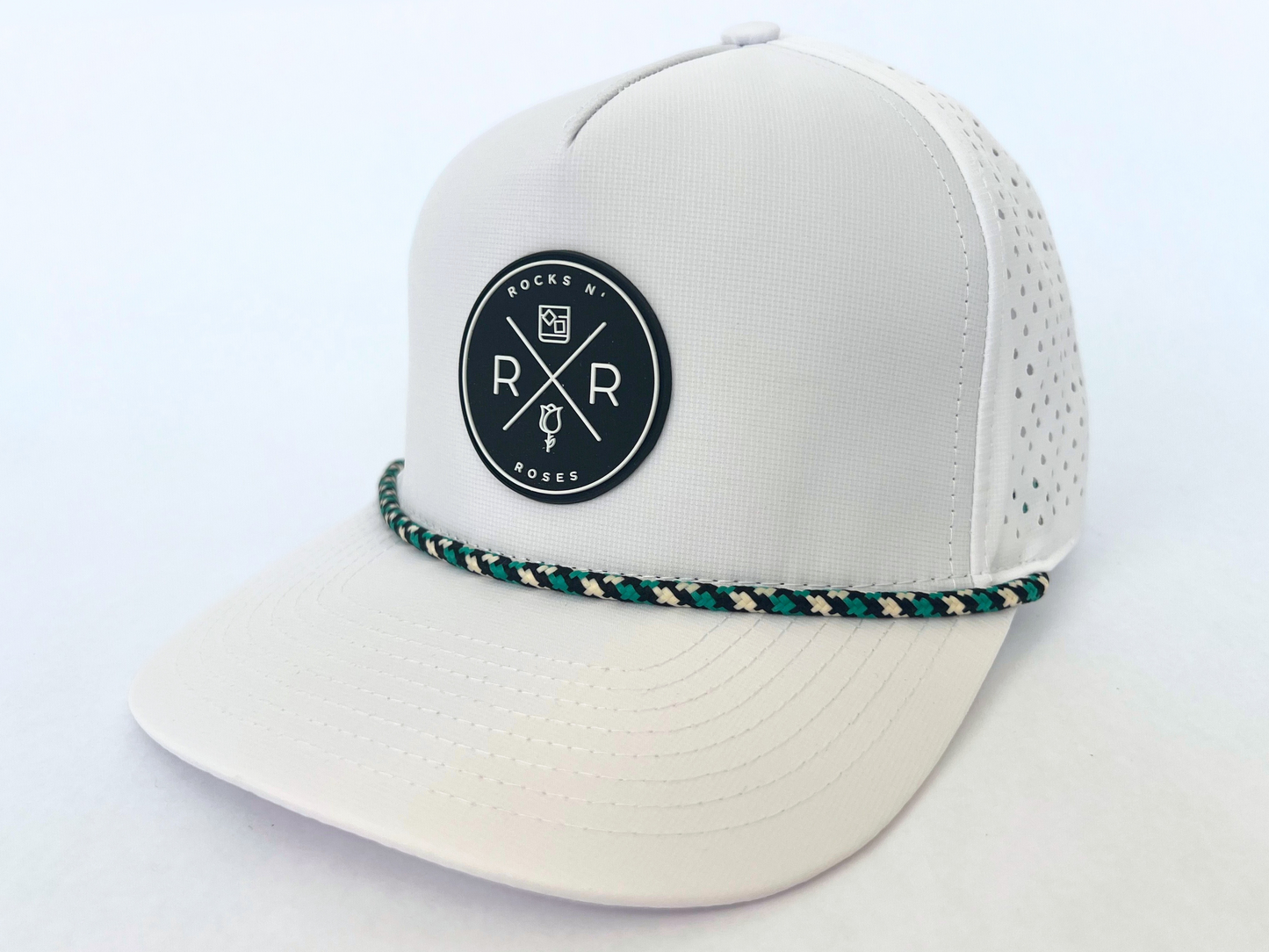 Close up shot of the Rocks N' Roses White Performance Golf Hat. This 100% polyester snapback hat is water resistant, offers some stretch and has that new school flat brim look. Also, it features a rubber logo and black, white, and teal rope that decorates the front brim. Laser cut venting for max breathability.