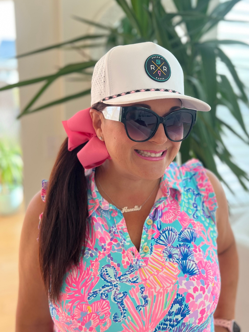 Photograph of a woman in a white women's golf hat by Rocks N' Roses featuring the Tropic Sunset PVC Rubber Logo and an pink and black rope