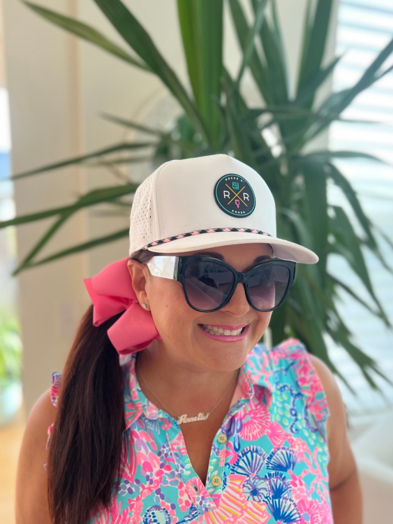 Photograph of a woman in a white women's golf hat by Rocks N' Roses featuring the Tropic Sunset PVC Rubber Logo and an pink and black rope