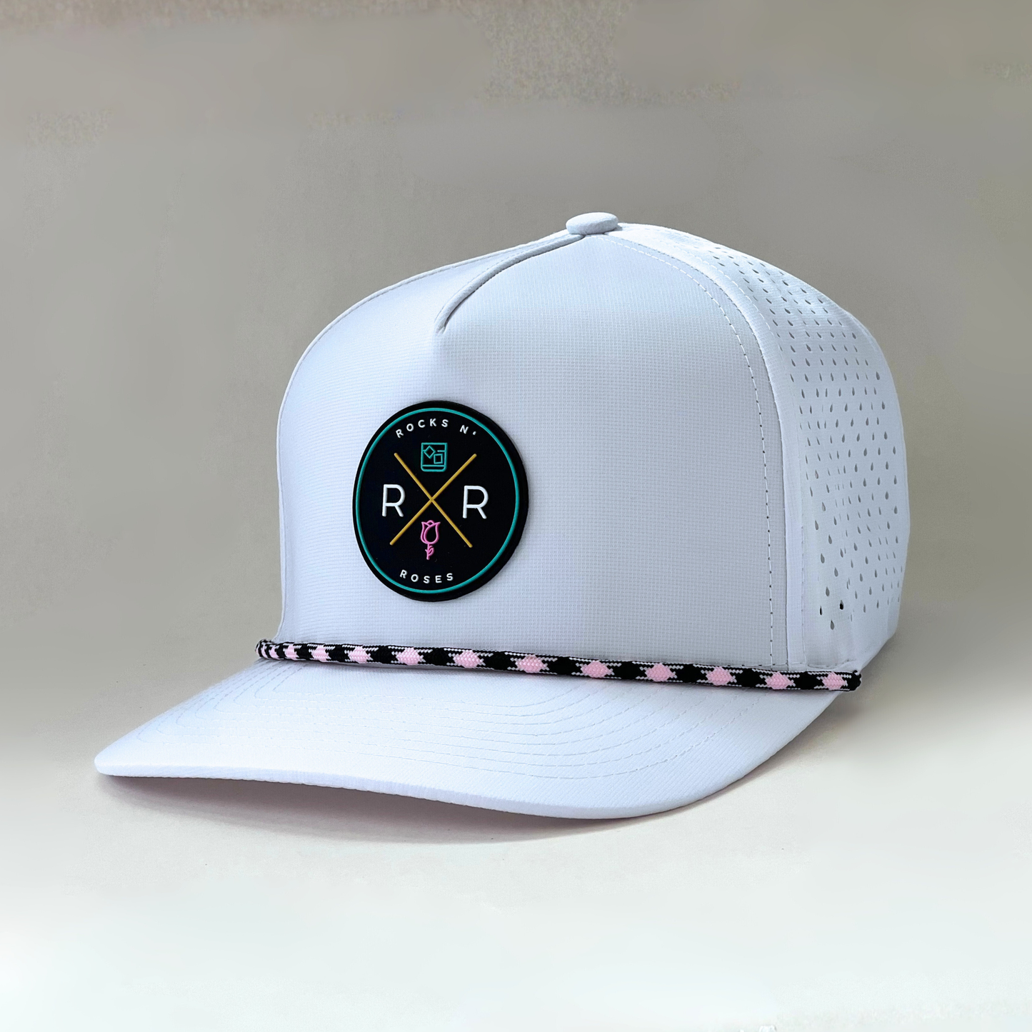 The new Rocks N' Roses Tropical Sunset Women's Golf Hat in White featuring a teal, pink, gold, white and black logo as well as a pink and black diamond rope.