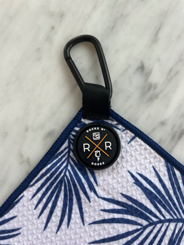 Close up shot of the Rocks N' Roses magnetic golf towel with a blue and white palm leaf pattern. Close up shows the magnet and carabiner for attaching to your golf bag.