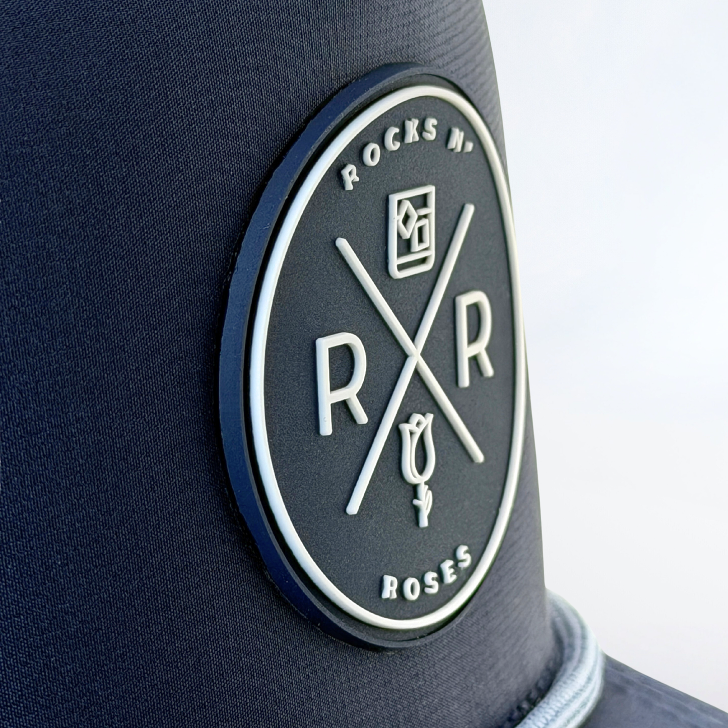 Close up of Rocks N' Roses navy blue golf hat 3D rubber molded logo in navy and white.