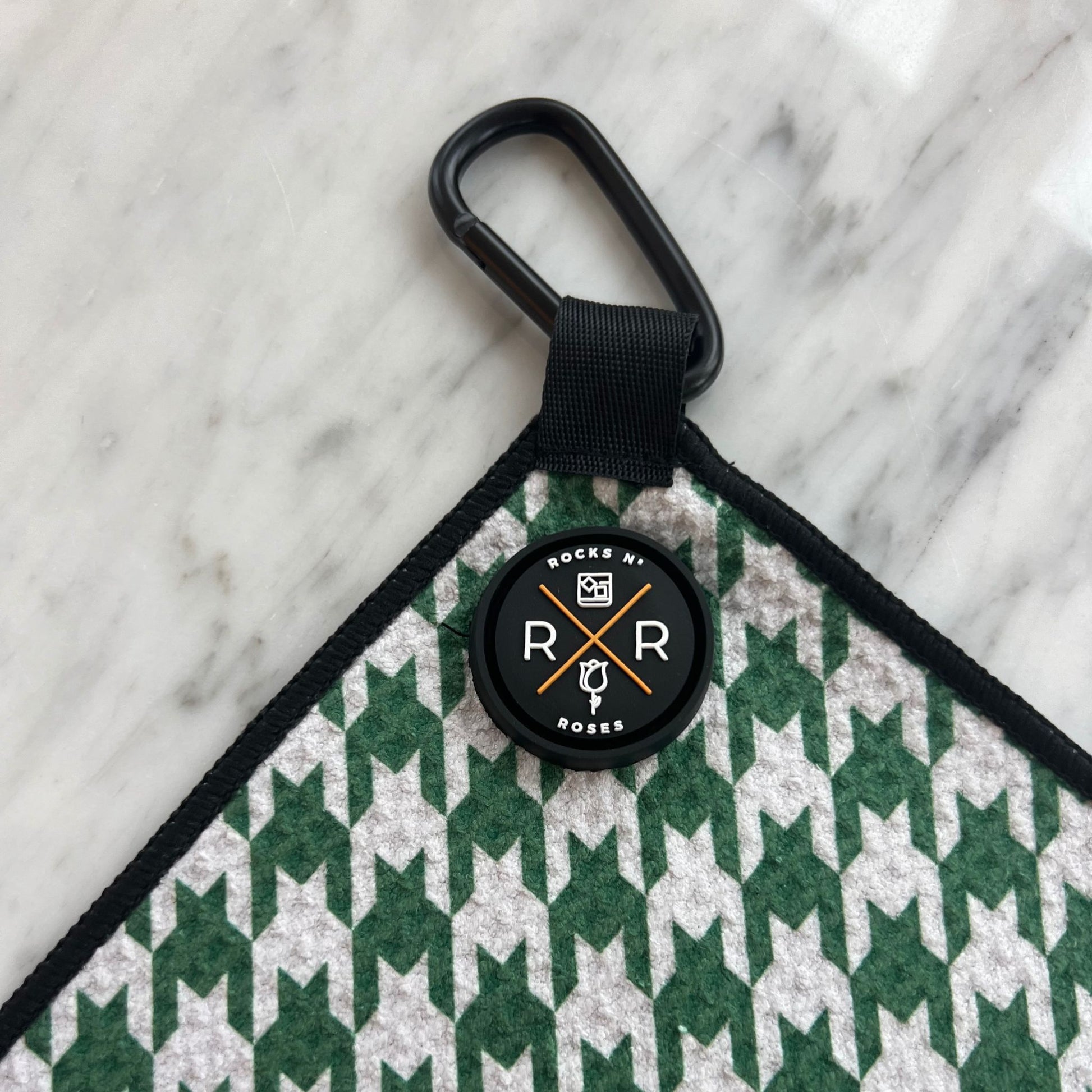 Close up shot of the Rocks N' Roses magnetic golf towel in a green and white houndstooth pattern. Close up shows the magnet and carabiner for attaching to your golf bag or golf cart.
