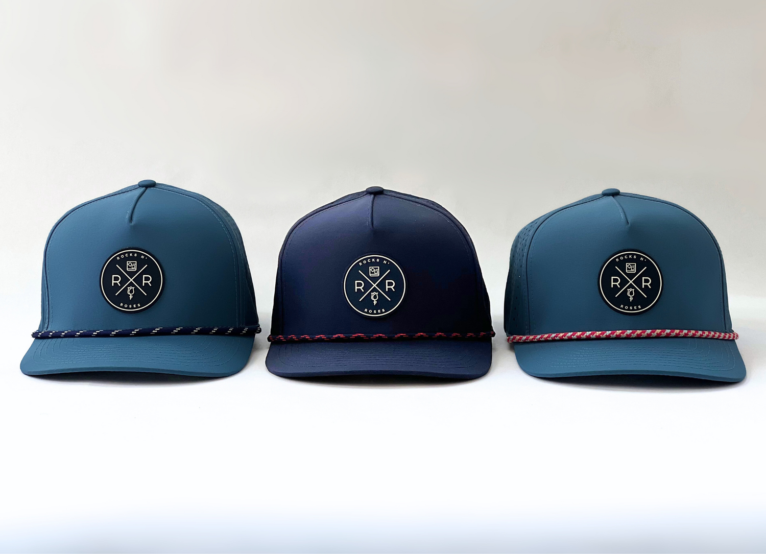 Image of three Rocks N' Roses Blue Golf Hats. Two light blue golf hats and a navy blue golf hat in the center. Each hat features a rubber logo and decorative rope.