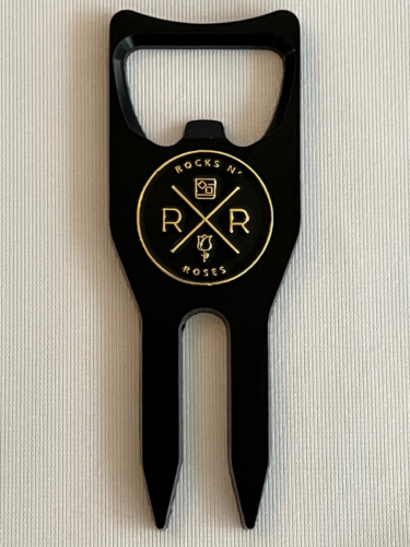 Image of the black and gold Rocks N' Roses Golf Multi-tool. This divot repair tool can not only be used to repair divots, it also includes a black and gold die-stamped ball marker and functions as a club rest and bottle opener.