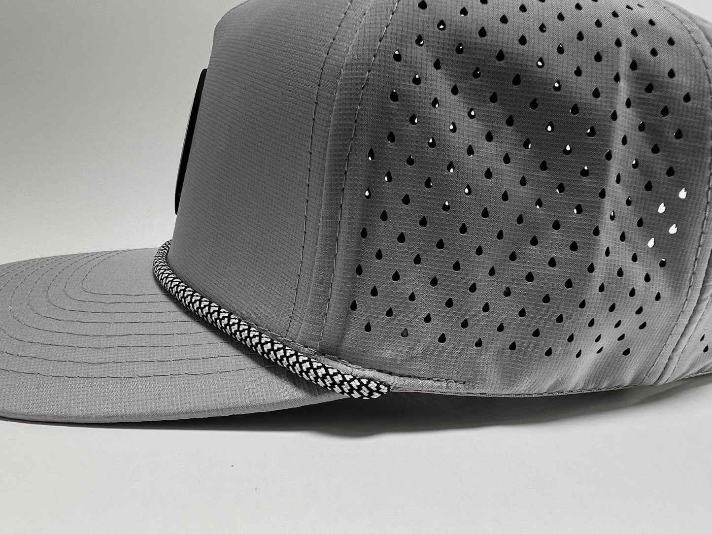 A close up shot of the side of the Rocks N' Roses Gray Golf Hat. This closeup shows the waterproof 100% polyester material used, later cut venting on the back four panels of the hat as well as the black and white checkered rope.