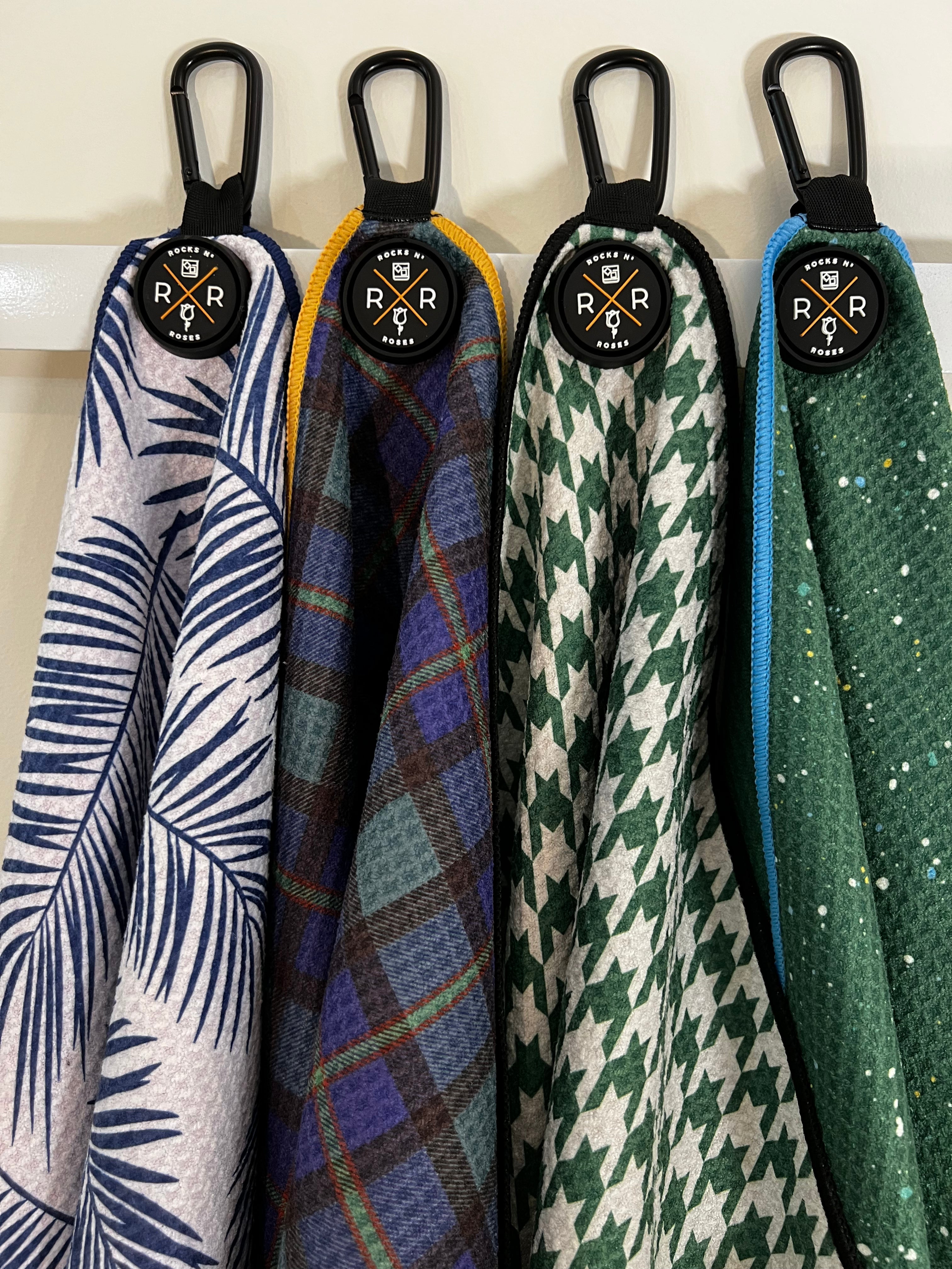 Image of the Rocks N' Roses Magnetic Golf Towel Collection which features four different designs. The blue and white palms, the Tartan, The Houndstooth and the pain splatter.