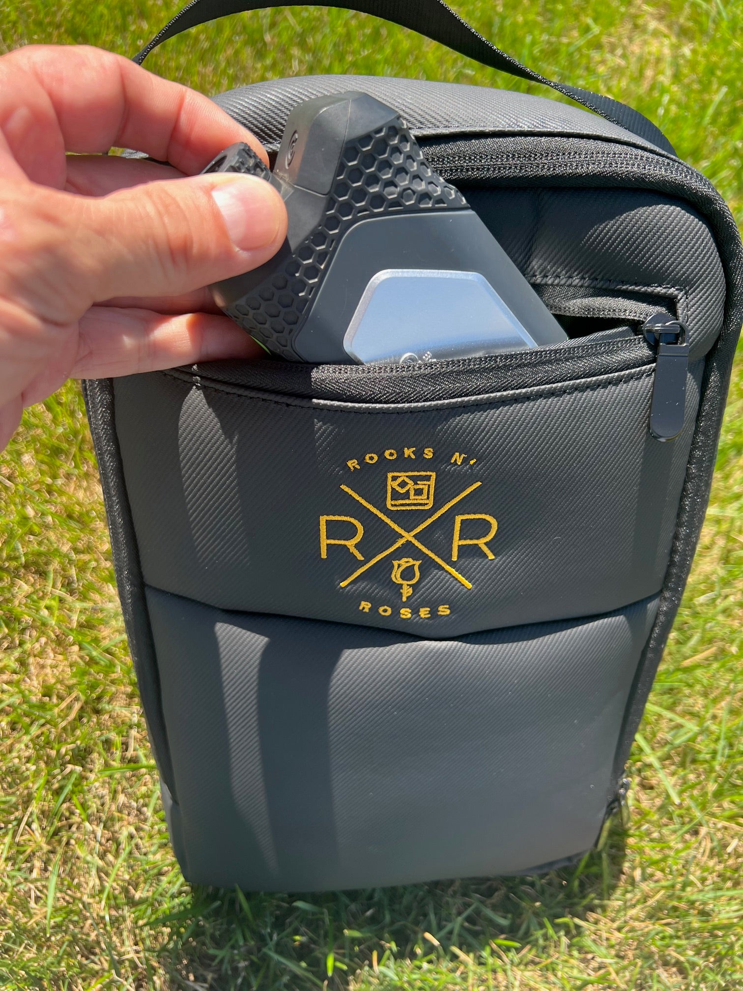 An image of someone placing a golf rangefinder into the valuables pocket of the black waterproof shoe bag by Rocks N' Roses.