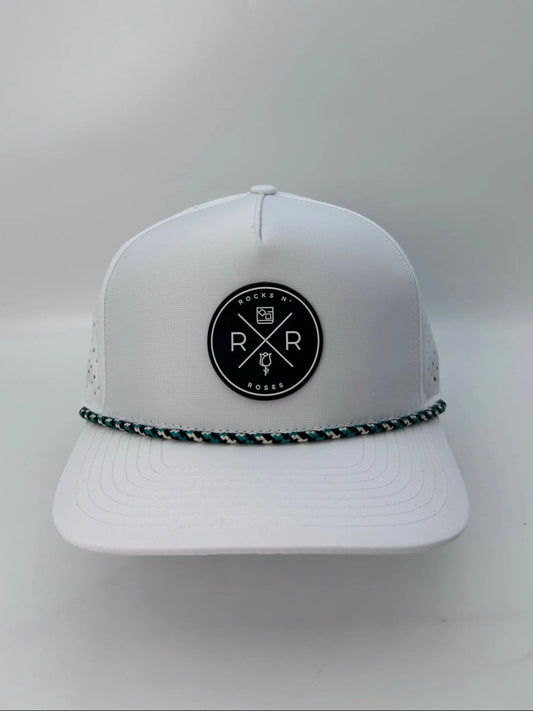 Image of the Rocks N' Roses 5 panel white golf hat. This performance hat is made of 100% polyester and is water resistant and has some stretch. It features a black and white circular rubber logo on the front and a black, white, and teal checkered rope.