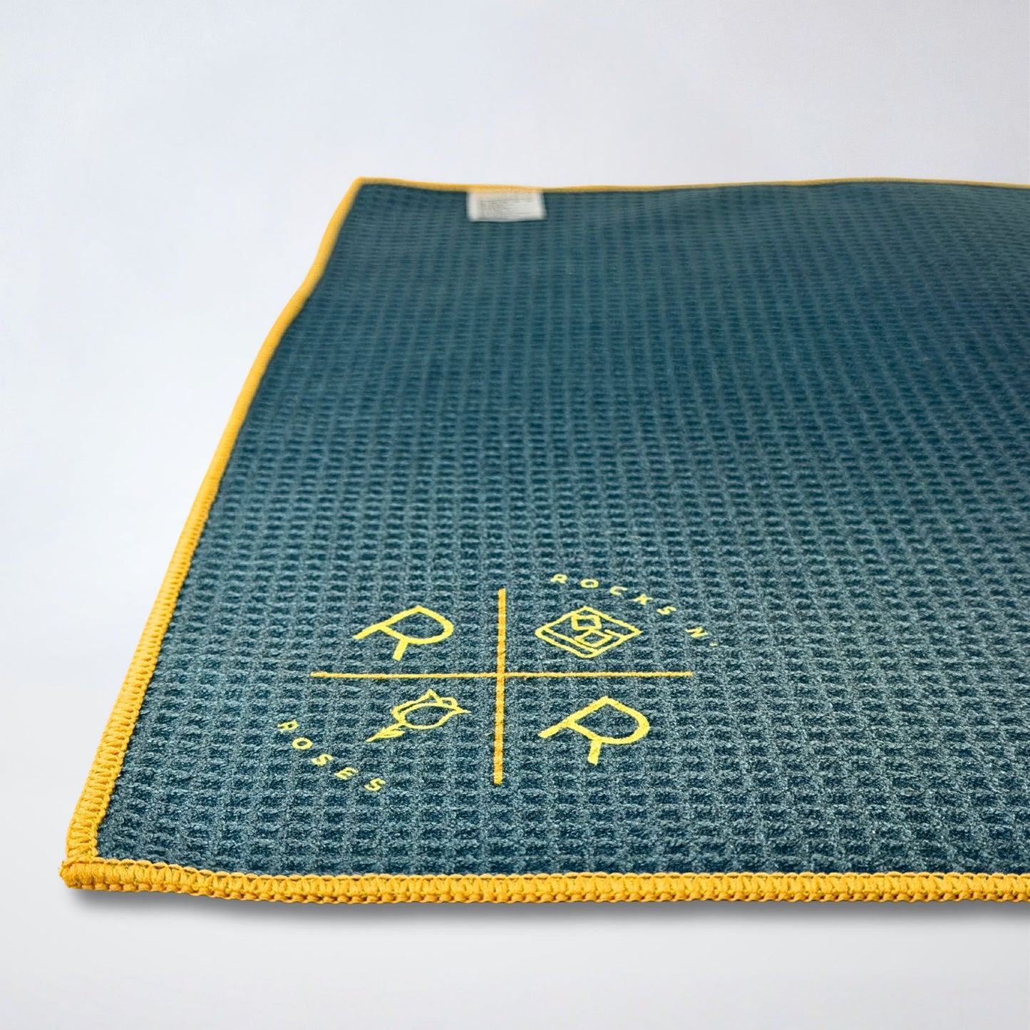 Close up photo showing a waffle weave golf towel part of the Rocks N' Roses Magnetic Golf Towel collection. Teal and blue tartan pattern with yellow gold.
