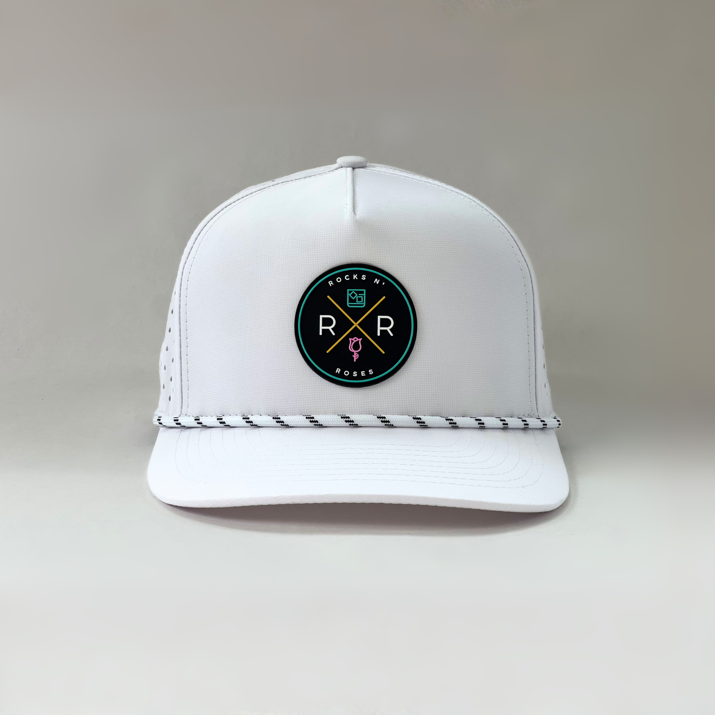 Image of a white golf hat made from 100% polyester with a teal, pink, and gold rubber Rocks N' Roses logo and white rope with a black accent.